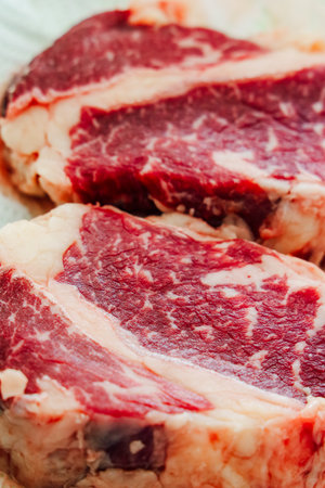 Two fresh marbled beef steaks sit on a wooden board showcasing their rich color and quality. Ideal for grilling or roasting.の写真素材