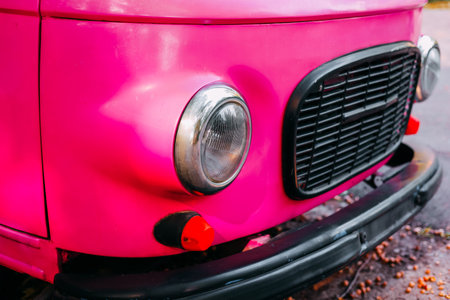 A vibrant pink vintage vehicle stands out with its distinct front design under clear skies.の写真素材