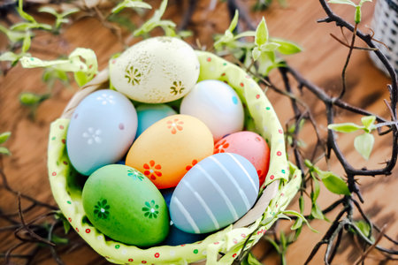 A basket filled with vibrant Easter eggs sits on a wooden surface adorned with fresh green leaves perfect for spring festivities.の写真素材