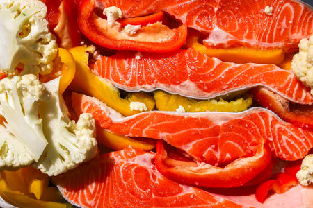 Brightly colored salmon fillets are arranged with sliced red and yellow bell peppers and cauliflower showcasing an appealing meal prep setup.の写真素材
