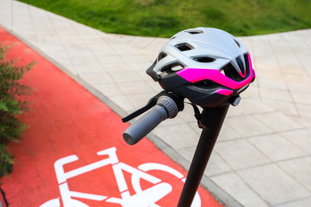 A vibrant bicycle helmet is mounted on a stand positioned near a designated bike lane in a park setting.の写真素材