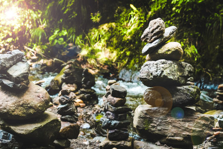 Different piles of stones are balanced near a clear river surrounded by vibrant green foliage reflecting peace and harmony.の写真素材