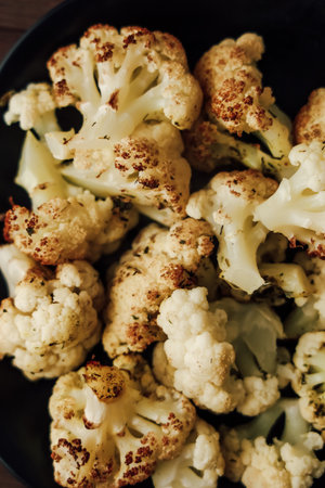 Golden roasted cauliflower florets seasoned for flavor are served in a black bowl showcasing their crispy texture.の写真素材