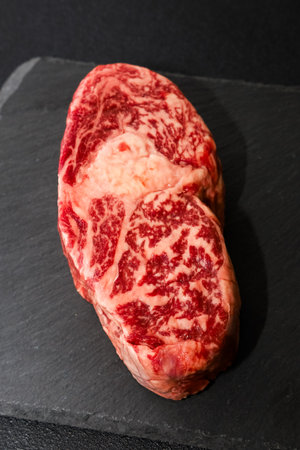 Marbled beef steak showcases rich textures and vibrant colors laying on a sleek black slate surface. Perfect for grilling or roasting.の写真素材