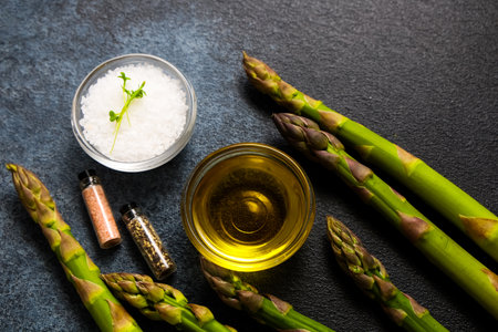 Bright green asparagus stalks are displayed alongside oil salt and a selection of spices showcasing ingredients for a nutritious meal.の写真素材