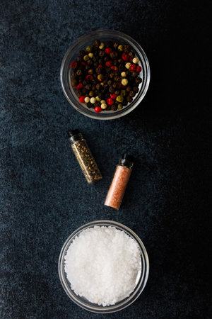 Colorful assortment of spices and salt displayed in glass containers on a dark textured surface showcasing culinary essentials for flavoring dishes.の写真素材