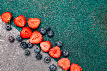 Vibrant red strawberries and deep blue blueberries are artistically placed on a textured background showcasing their freshness and appeal.の写真素材
