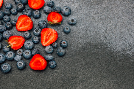 A vibrant display of sliced strawberries and whole blueberries pops against a dark background highlighting their freshness.の写真素材