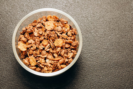 A mixture of crunchy and sweet granola is displayed in a clear bowl on a dark background perfect for healthy breakfasts and snacks.の写真素材