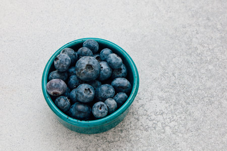 A turquoise bowl filled with freshly picked blueberries sits on a light-colored textured surface showcasing their vibrant color and freshness.の写真素材