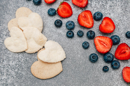 Soft heart-shaped cookies alongside vibrant strawberries and blueberries create a delightful dessert arrangement.の写真素材