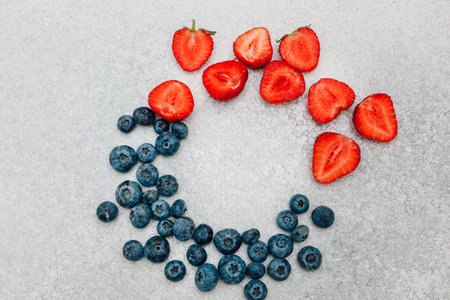 Vibrant strawberries and blueberries are artfully arranged in a circular design on a light gray...