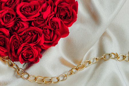 Beautiful red roses are artistically arranged on a soft creamy fabric complemented by a delicate gold chain.の写真素材