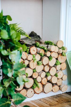 A neatly arranged stack of wooden logs with lush greenery accents provides a refreshing touch to...