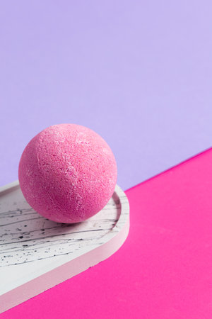 A bright pink bath bomb rests on a minimalist wooden tray contrasting with purple and pink backgrounds creating a serene atmosphere.の写真素材
