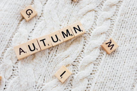 Wooden letter tiles arranged to form the word autumn on a warm textured cream sweater. The soft...
