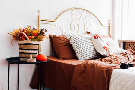This inviting bedroom features a golden bed frame earthy brown bedding autumnal floral arrangements and cozy pillows.の写真素材