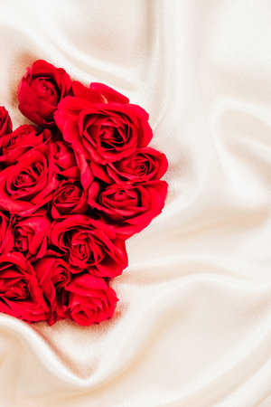 Beautiful red roses are arranged in a heart shape on delicate cream fabric creating a romantic and elegant display suitable for special occasions.の写真素材