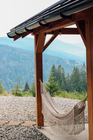 A cozy hammock hangs beneath a wooden shelter providing a perfect spot for relaxation. Majestic mountains and dense trees offer a serene backdrop.の写真素材