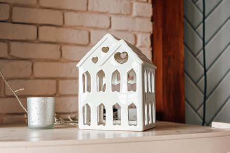 A ceramic house shaped lantern sits on a shelf complementing a cozy room with soft lighting and warm tones ideal for a peaceful atmosphere.の写真素材