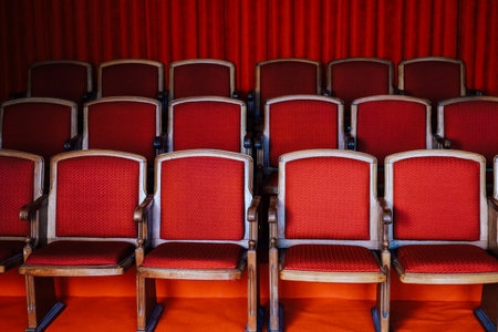 Red upholstered chairs are neatly arranged in rows within a theater ready for audience members who will enjoy a performance.の写真素材