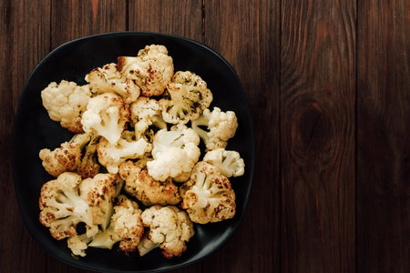 Fresh cauliflower florets are roasted to a golden brown arranged neatly in a black bowl. Perfect for a healthy dish.の写真素材