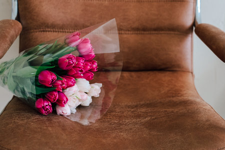 Colorful tulips are placed casually on a brown leather chair creating a warm and inviting atmosphere. The setting exudes tranquility and charm.の写真素材