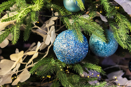 Decorative blue ornaments hang gracefully on an evergreen tree surrounded by shiny leaves and twinkling lights creating a festive atmosphere.の写真素材