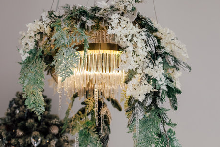 A unique chandelier adorned with lush greenery and delicate white flowers illuminates a cozy room setting a festive atmosphere.の写真素材