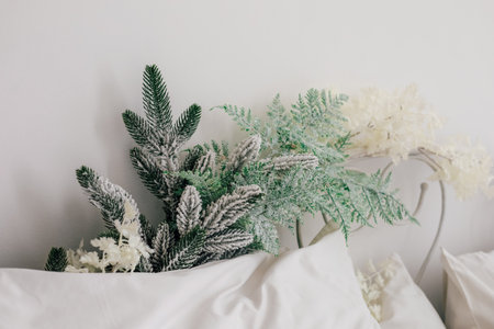A winter foliage arrangement featuring green pine and frosted branches greets viewers atop soft white bedding creating a seasonal vibe.の写真素材