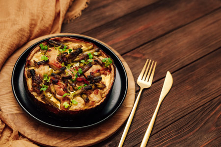 quiche pie vegetable dish sits on a wooden plate beside shiny cutlery. The blend of colors and textures invites enjoyment during a meal.の写真素材