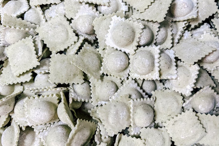A variety of spinach filled ravioli lie stacked together showcasing their unique shape and texture waiting to be cooked in a cozy kitchen setting.の写真素材