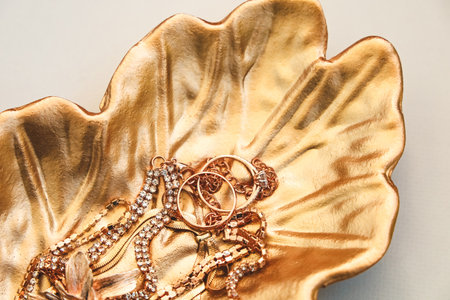 A beautifully crafted golden leaf shaped dish contains various shimmering jewelry items including necklaces and rings arranged attractively.の写真素材