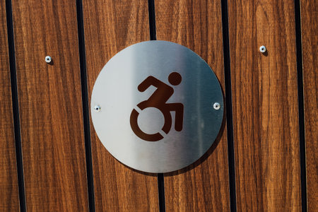 A metal sign mounted on a wooden surface indicates an accessible entrance for those using wheelchairs. It promotes inclusivity and accessibility.の写真素材