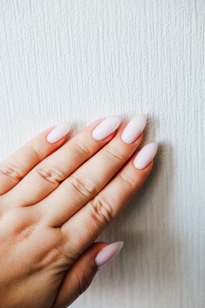 A hand with long polished nails rests gently against a textured wall showcasing a soft pastel manicure in natural light.の写真素材
