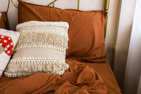 A cozy bedroom showcases a warm brown bedspread paired with textured pillows creating a serene atmosphere during the day.の写真素材