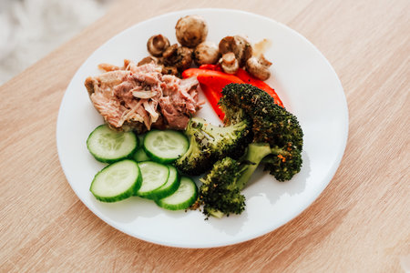 A nutritious meal showcases grilled chicken with cucumber slices broccoli red pepper and sauted mushrooms on a plate.の写真素材