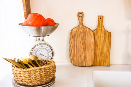 Fresh red tomatoes rest in a metal bowl on a scale next to wooden cutting boards and utensils in a cozy kitchen.の写真素材