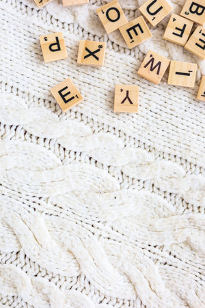 Colorful wooden letters are scattered across a textured white knitted blanket creating a playful...