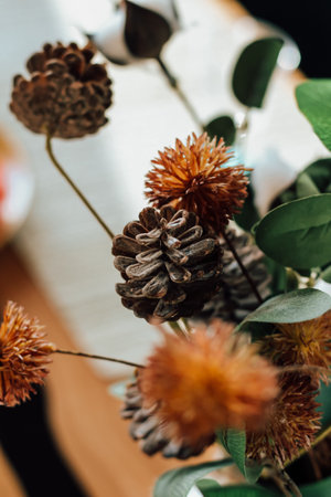 Arrangement features dried flowers and pinecones in a warm indoor environment. Natural elements create a rustic and inviting atmosphere.の写真素材