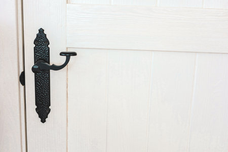 Close up view of a decorative black handle and latch on a white wooden door showcasing classic design elements in a well lit space.の写真素材