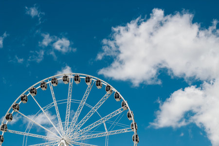 A large Ferris wheel stands tall against a bright blue sky dotted with fluffy white clouds during a sunny afternoon.の写真素材