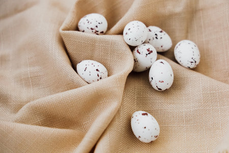 Small speckled quail eggs are neatly placed on a light beige cloth showcasing their delicate beauty and unique patterns.の写真素材