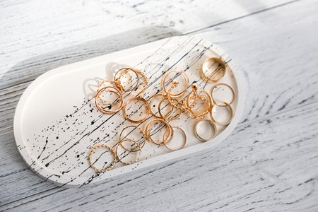 Gold rings are neatly arranged on a modern tray featuring a minimalist design placed on a light wooden surface with natural lighting.の写真素材