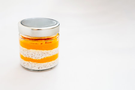A glass jar showcases a visually appealing layered dessert with bright orange and creamy white stripes. The texture invites tasting.の写真素材