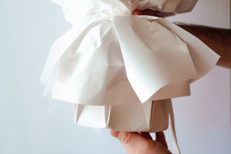 A hand carefully holds a wrapped gift box in white paper showcasing anticipation and joy. The soft indoor light creates a warm atmosphere.の写真素材
