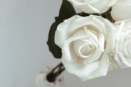 A close up view of fresh white roses arranged in a clear vase showcasing their delicate petals and green leaves enhancing the calm atmosphere.の写真素材