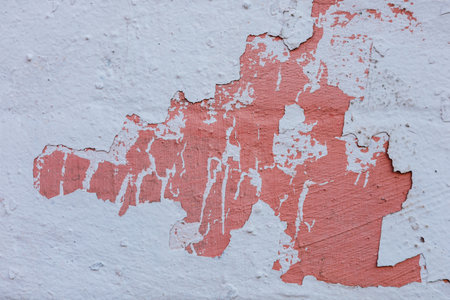 A weathered wall shows layers of peeling paint revealing an undercoat of pinkish hues and a textured surface indicating age and neglect.の写真素材