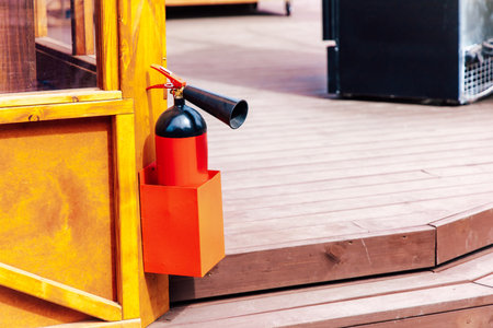 A fire extinguisher is securely attached to a wooden structure in an outdoor seating area ensuring safety and accessibility for patrons.の写真素材