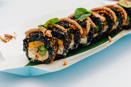 A vibrant sushi roll fills a plate showcasing layers of black rice vegetables and unique toppings ready to be enjoyed at lunchtime.の写真素材